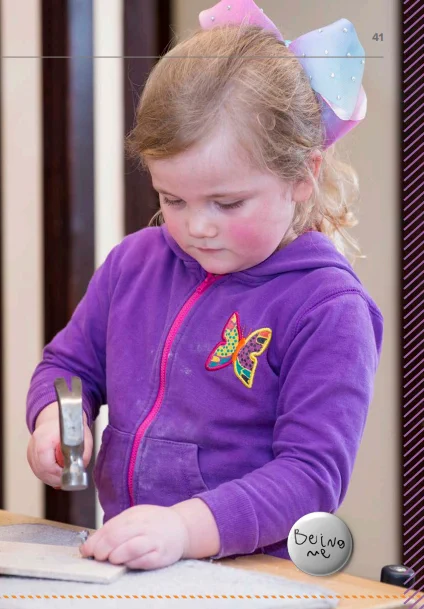 Young child holding a hammer and hitting a nail into wood. 
