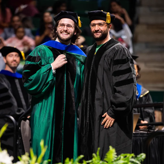 After the hooding ceremony, a doctoral student and their advisor smile for a picture