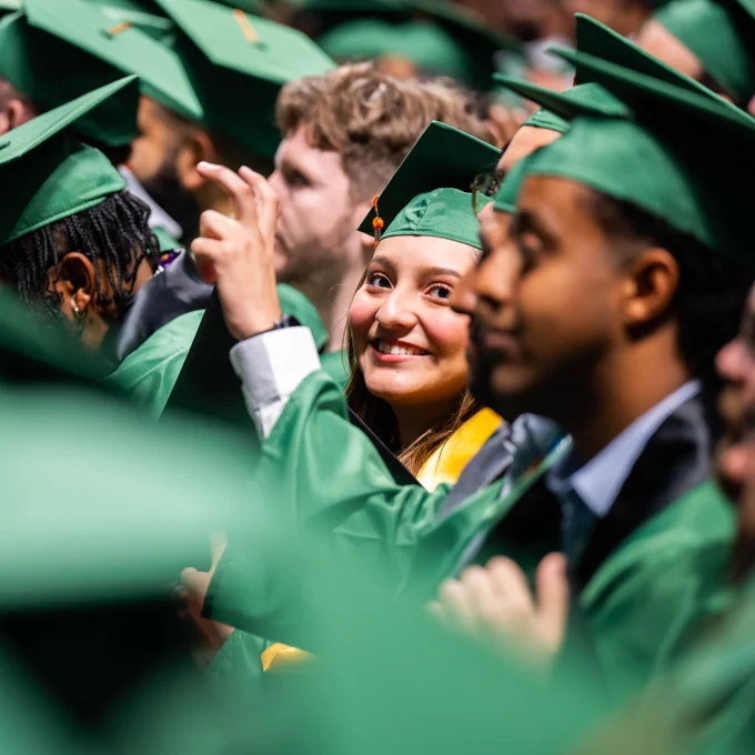 Multiple bachelor students sit in their seats, and one student turns and smiles for a picture.
