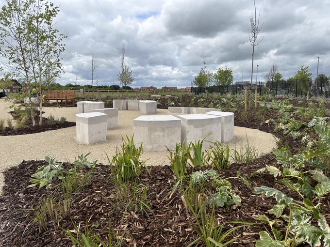 a garden with stone and terrazzo block benches in a circle surrounded by newly planted gardens
