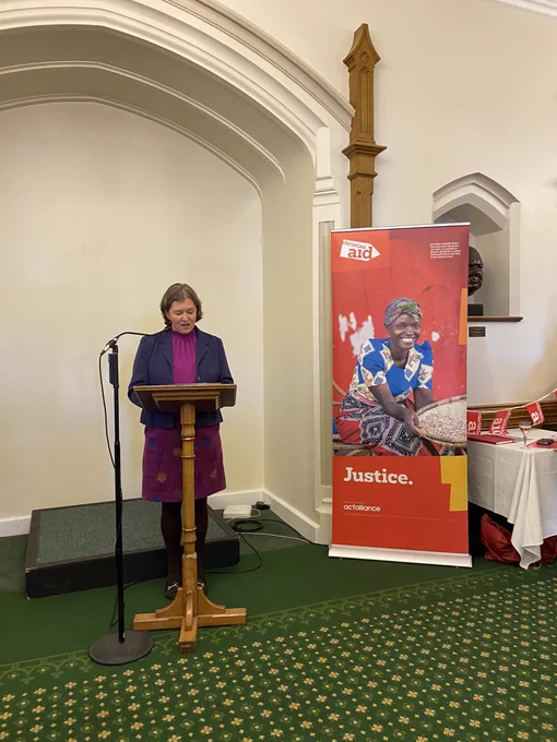 Fleur Anderson stands at a lectern next to a Christian Aid banner