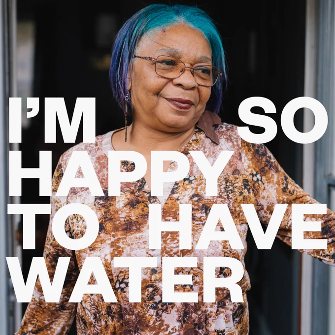 Portrait of Donna standing in her doorway. White text: I'm so happy to have water.