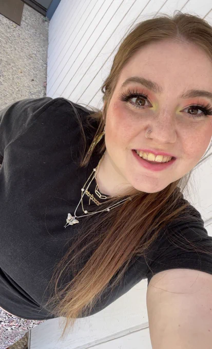 A woman in a black tshirt taking a selfie, smiling at the camera with long auburn red hair