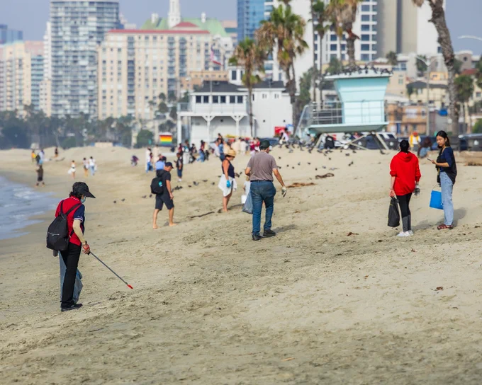Beach cleanup in Long Beach. Multiple people of all ages gathering with bags to pick up trash from the beaches.