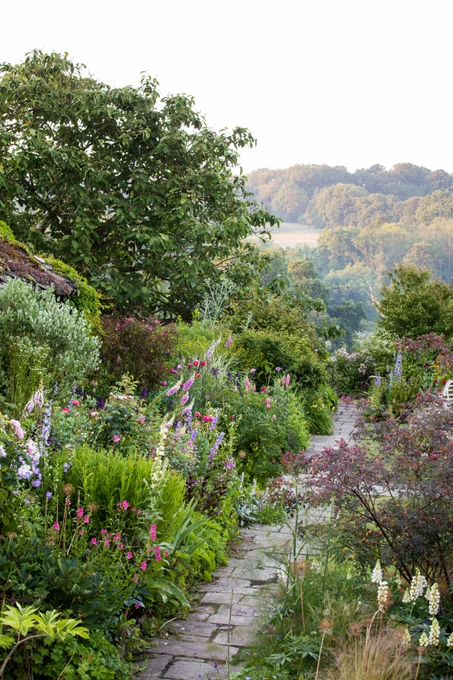 A photograph of a naturalistically planted garden with a path running through the middle and trees in the distance.