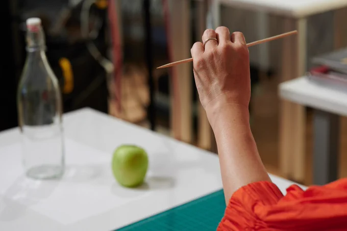 Close-up of a person holding up a small dowel to measure while drawing