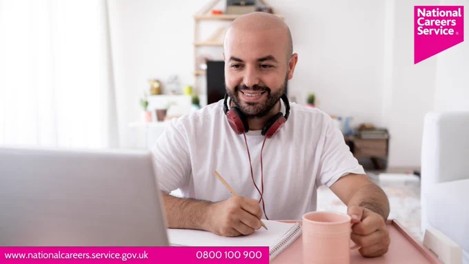 A man sat at a desk with a notebook, headphones and a mug doing some online learning. Top right is the National Careers Service logo and bottom left reads: "www.nationalcareers.service.gov.uk / 0800 100 900".