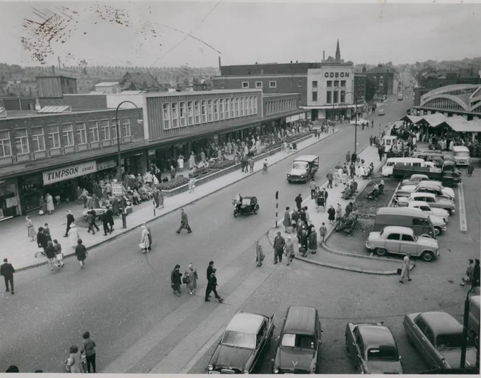 Black and white photo of Broadway, Accrington (before the Town Hall extension c. 1960s), There are cars parked to the right, and people crossing the road and on the pavements in the centre and to the left of the image