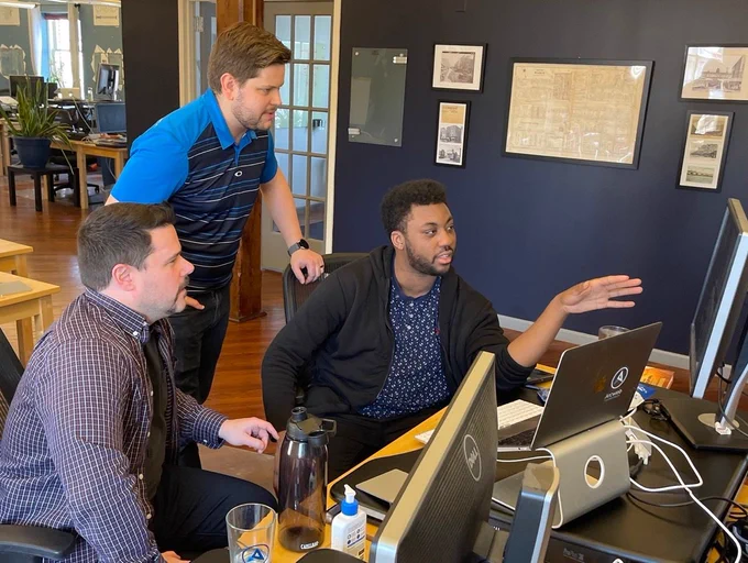 Three male technologists looking at a computer monitor in an office.