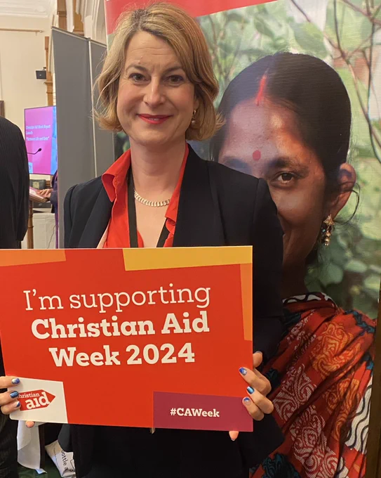 Helen Hayes MP carrying a placard which reads ‘I’m supporting Christian Aid Week 2024’