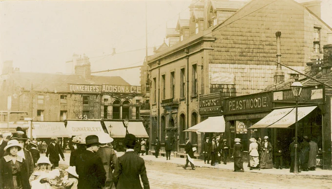 Sepia photo of Manchester Road, Burnley (c. 1913) showing shops and people standing in the street