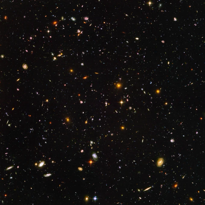 Hubble Ultra Deep Field. The image is filled with galaxies in colors of white, yellow, blue-white, and red, all on a black background.