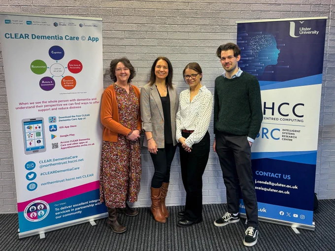 Four people standing together with a pop-up banner in place to the left and right of them