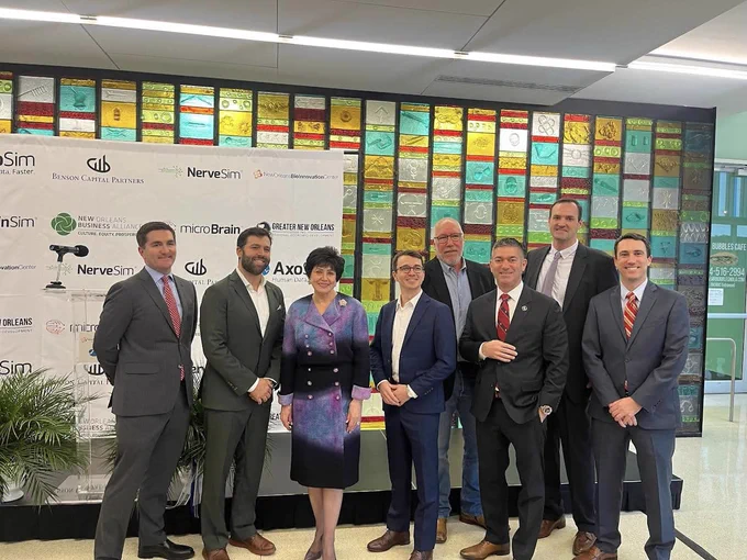 Eight people posing in front of a wall with various corporate logos at a formal event. One of the featured people is Gayle Benson, owner of the New Orleans Saints.