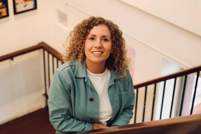 Writer Kayleigh Llewellyn is standing on a flight of stairs at Chapter Arts Centre. She is smiling towards the camera