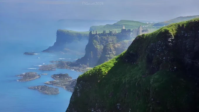 A photograph of Dunluce Castle ruins on top of a cliff with the sea with sea mist hanging in the air 