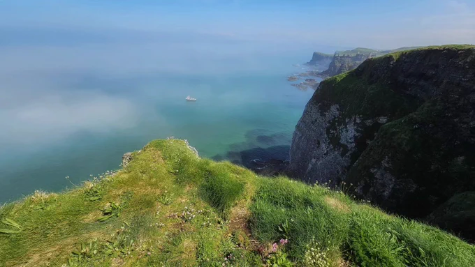 A different view from the cliff of the sea with a boat in the picture 