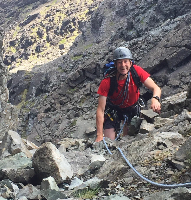 Park Authority Head of Visitor Services and Active Travel, Colin Simpson, smiling at the camera while rock climbing in the Cairngorms National Park.
