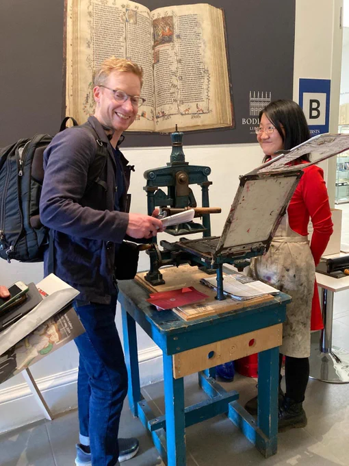 A book fair visitor tries out the Bodleian printing press, overseen by an expert
