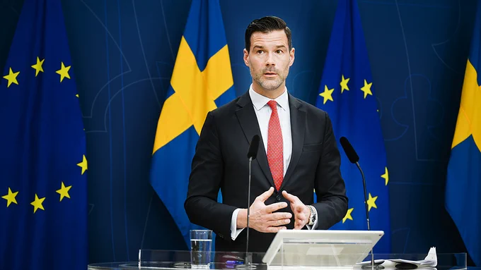 Forssell talks during a press conference. Standing in front of the Swedish flag and the EU flag.