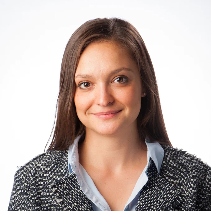 Headshot of Sarah Glozer in a tweed jacket and light blue shirt, smiling against a white background.