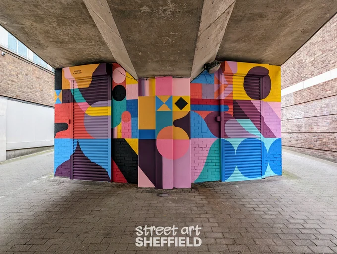 Colourful abstract mural of different shapes on a wall and shutters below a ramp leading up to a car park