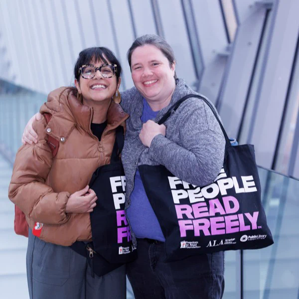 Photo: Two people smile and pose with their purple FPRF tote bags. Photo courtesy of Kinser Studios. 