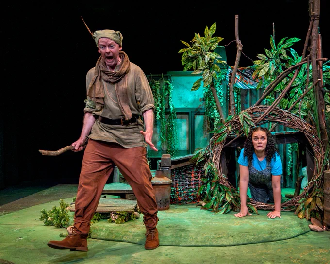 Two people on a set that looks like a den in a forest.