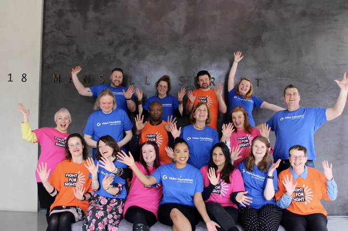 A team photo of people smiling, waving, and wearing alternating Vision Foundation and Fight for Sight t-shirts.