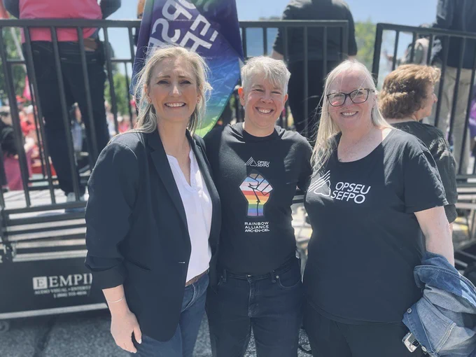 A group photo of smilling union leaders. From left to right: Ontario Federation of Labour President Laura Walton wearing a black blazer and white blouse, OPSEU/SEFPO President JP Hornick wearing a black t-shirt with a solidarity fist in the colours of the pride flag, and OPSEU/SEFPO First Vice President & Treasurer Laurie Nancekivell wearing a black t-shirt with the OPSEU/SEFPO logo.