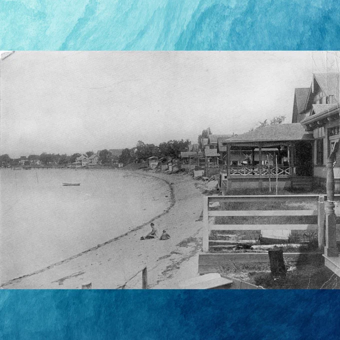 A black and white photograph of beach houses lining the shore. The houses are on the right side of the photograph and the beach and water are on the left. There are two people sitting on the beach in the distant background. The background of the post is a watercolor blue paint background.