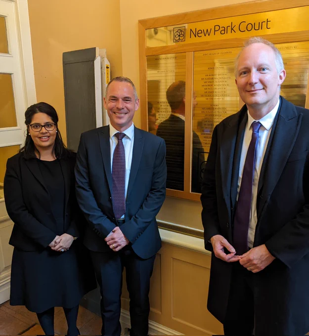 Amrit Kaur Dhanoa, Rob Wagg, and Sam Townend KC standing in the entrance of New Park Court chambers in front of a gold sign with New Park Court members listed 