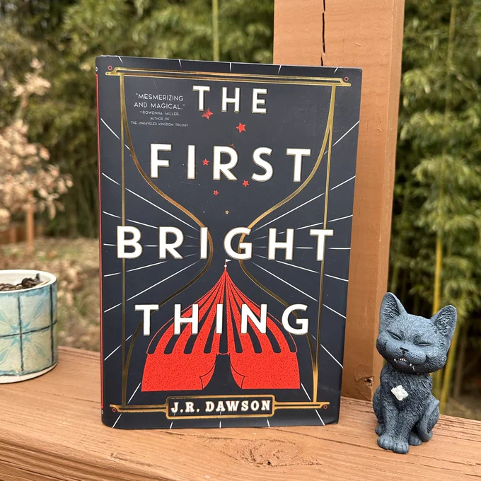 The First Bright Thing by J.R. Dawson is photographed beside a small black cat figurine 