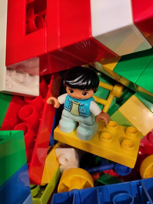 A lego figure sat on a pile of multi coloured lego pieces.