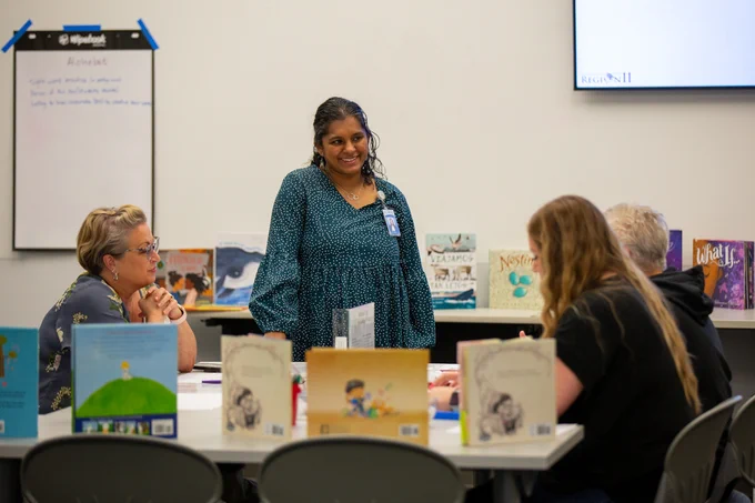 Two educators share their hand-drawn instructions for creating a PB&J sandwhich. One leans over to table, listening intently, while the the other shares her ideas.