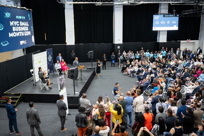 Overhead shot Mayor addressing crowd and people sitting on stage while addressing crowd on the right.