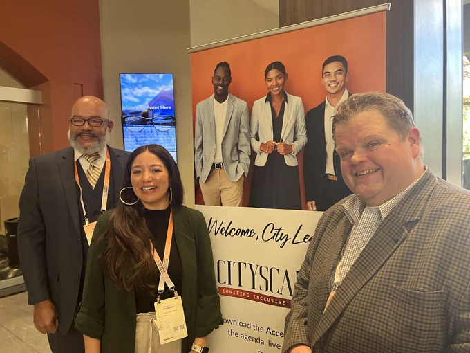 Two men and a woman smile next to a pop-up sign reading "Welcome, City Leaders."