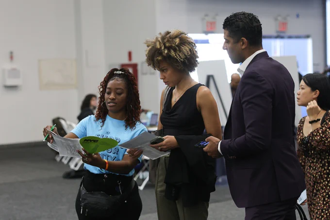 Woman in blue shirt pointing at map with two people by her side.