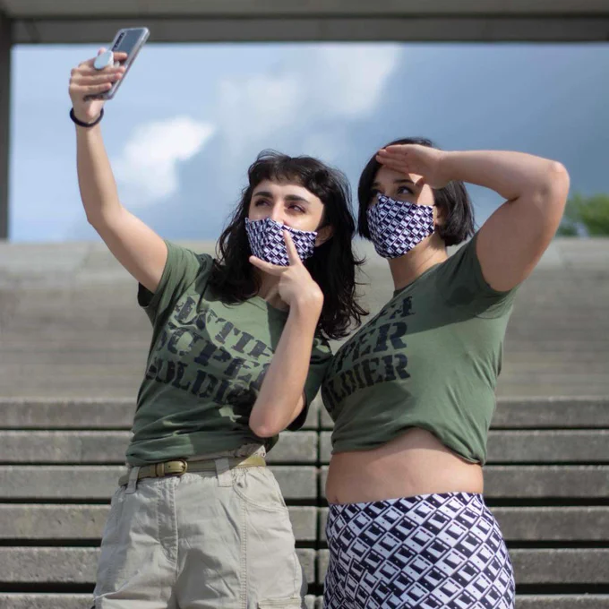 Two women wearing T-shirts that say antifa super soldier. One is saluting and the other one is taking a selfie.