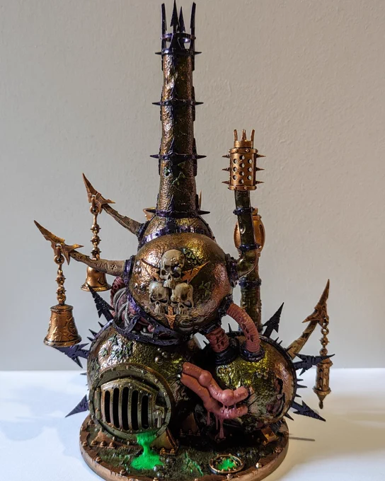 Detailed model of a fantastical tower featuring a blend of Gothic and industrial styles, with metallic textures, spikes, and various ornaments including skulls, chains, and bells. The structure is set on a circular base, and exhibits a dark palette with green glowing elements.