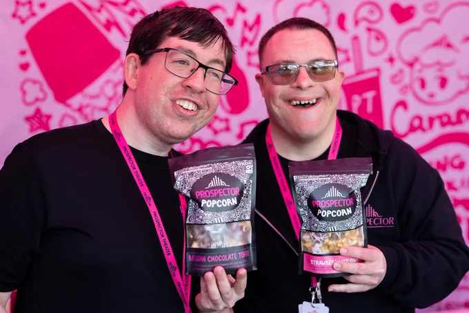 Dillon and EJ smile while holding up popcorn bags at a popup event.