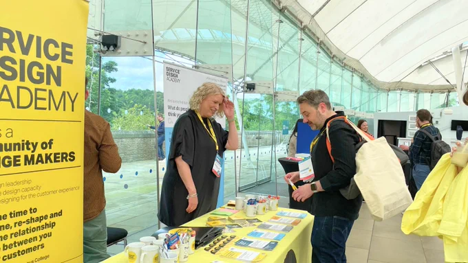Two individuals are engaged in conversation at the Service Design Academy sponsor stand inside Dynamic Earth.