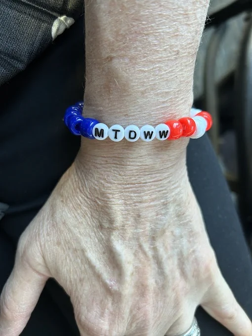 Photo of a person's hand that has a red, white and blue beaded bracelet around their wrist. The white beads display black letters that read: MTDWW