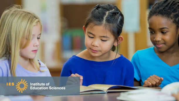 Three young girls reading together in a library. To their left is   the Institute of Education Sciences (IES) logo.