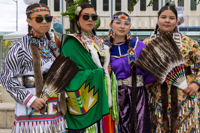 Four powwow participants wearing colourful regalia stand next to each other in Churchill Square.