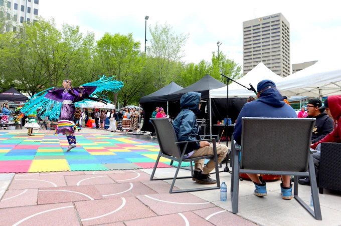 A powwow dancer in colourful regalia spins in Churchill Square next to a circle of drummers.