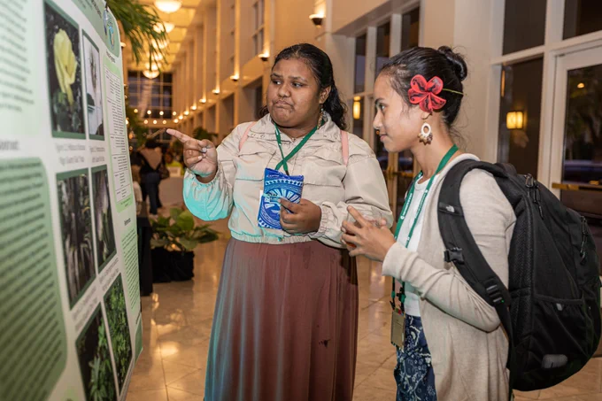 Two people stand in front of a research poster. One is pointing to one of the charts on the poster. 