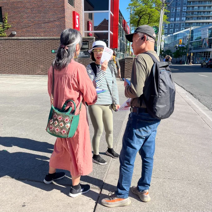 Three people are having a conversation, one person is holding  clipboard, the other two have just taken a leaflet.
