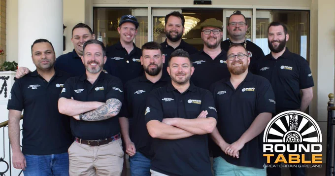A photo of members of Round Table, wearing black branded t-shirts, arms folded and smiling to camera