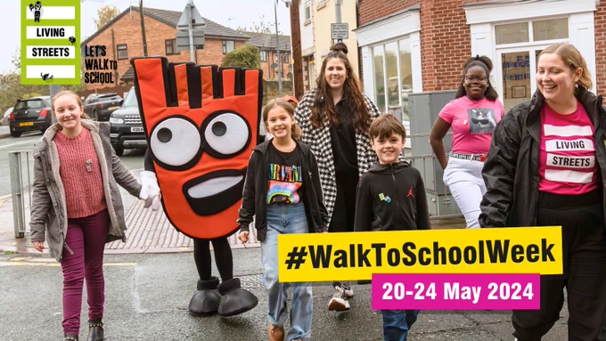 A group of schoolchildren cross the road with a teacher, Strider (Living Streets' foot-shaped orange mascot) and a woman wearing a Living Streets T-shirt. On the graphic are the Living Streets and Let's Walk to School logos, the hashtag #WalkToSchoolWeek and 20-24 May.

